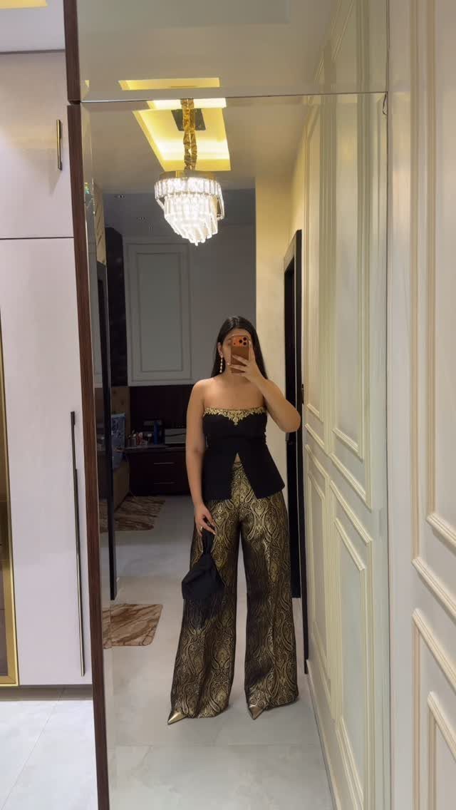 Woman wearing a black peplum crop top and gold metallic wide-leg palazzo pants.