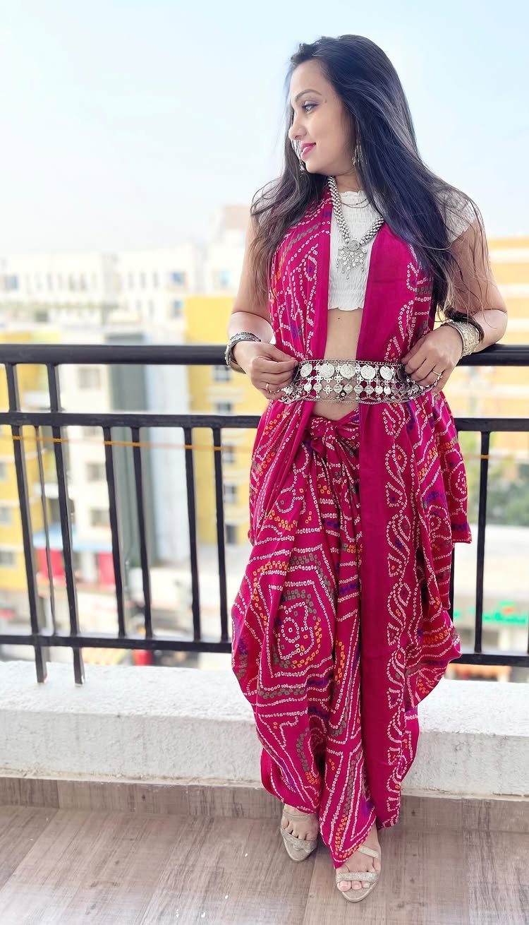 Woman wearing pink patterned dhoti pants, white crop top, and matching long jacket.