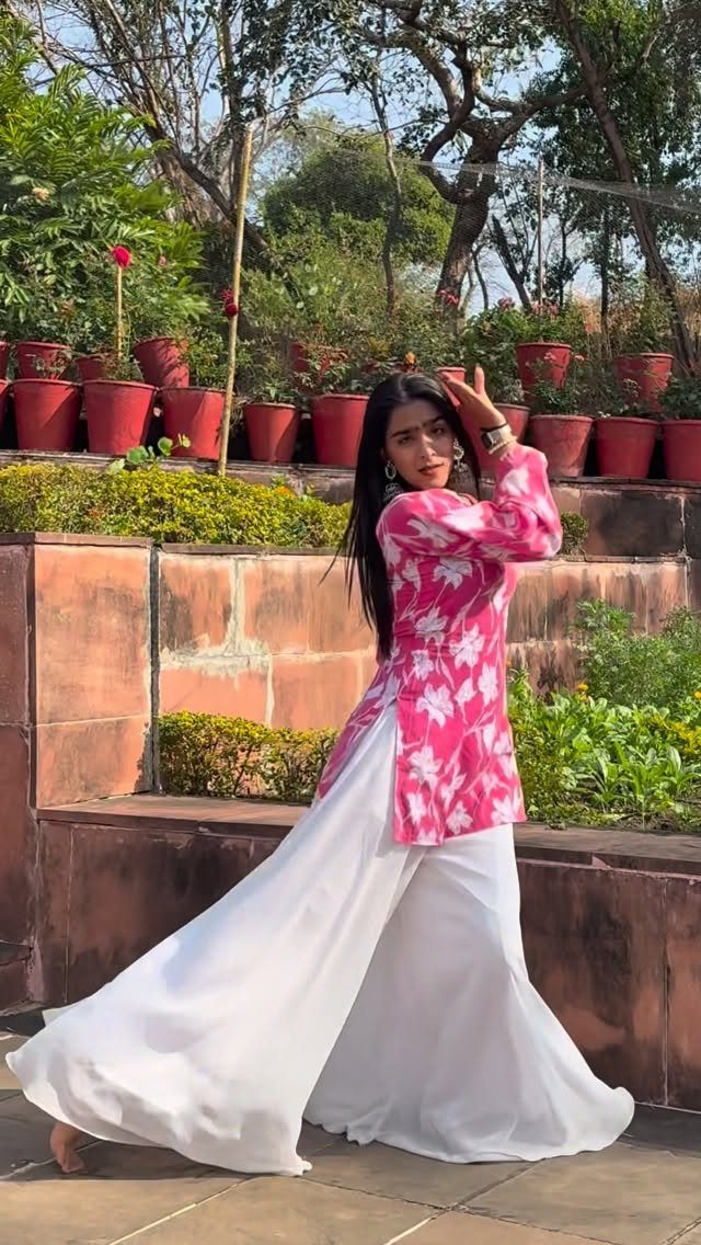 Woman wearing a pink floral long jacket and white wide-leg palazzo pants outdoors.