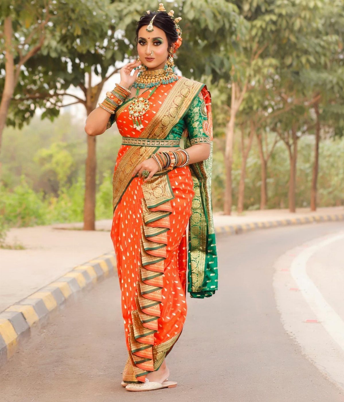 Woman wearing a traditional orange and green Maharashtrian Nauvari saree with gold jewelry.