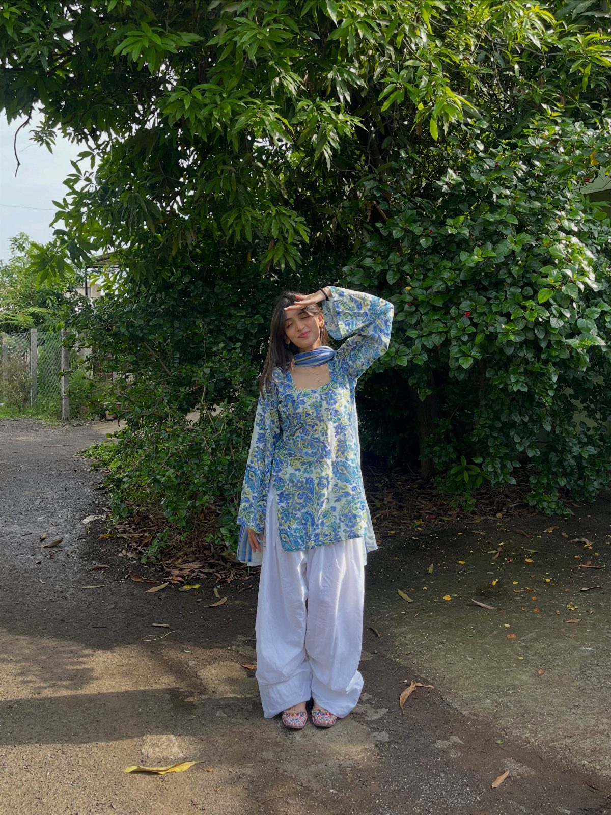 Woman wearing a blue floral short kurti and white pleated salwar pants outdoors.