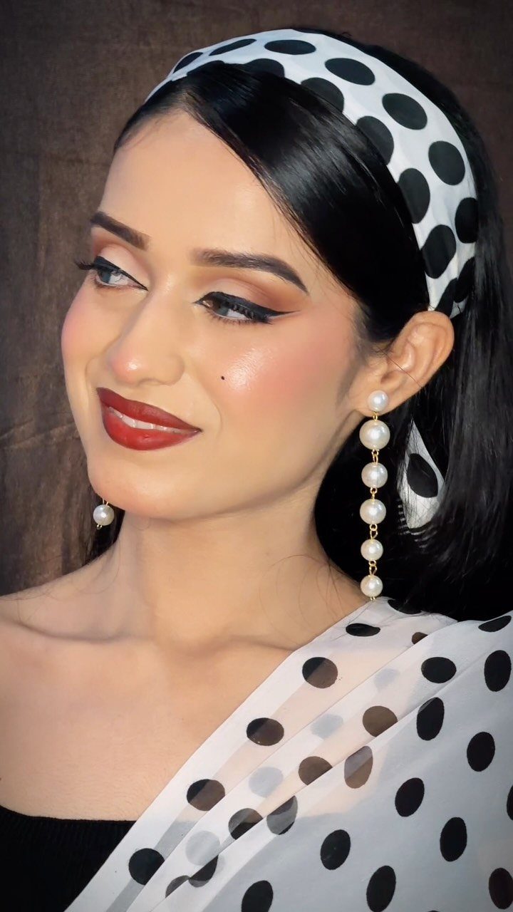 Woman wearing a white polka dot saree and headband with retro Bollywood makeup.