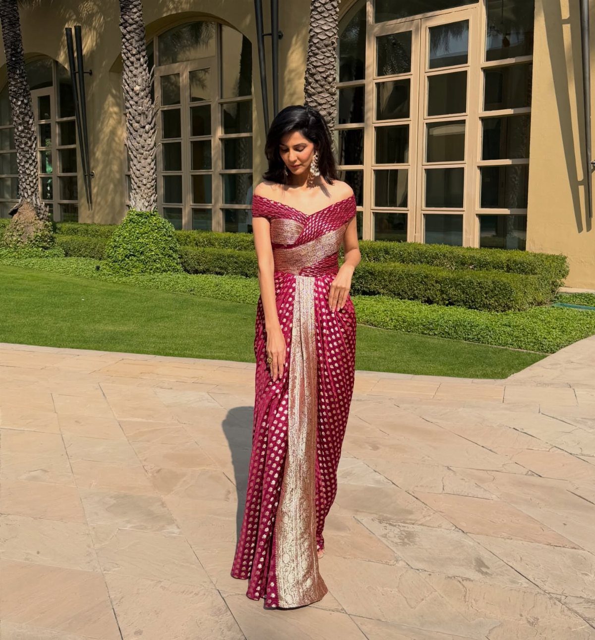 Woman wearing a magenta and gold saree gown standing on a stone patio.