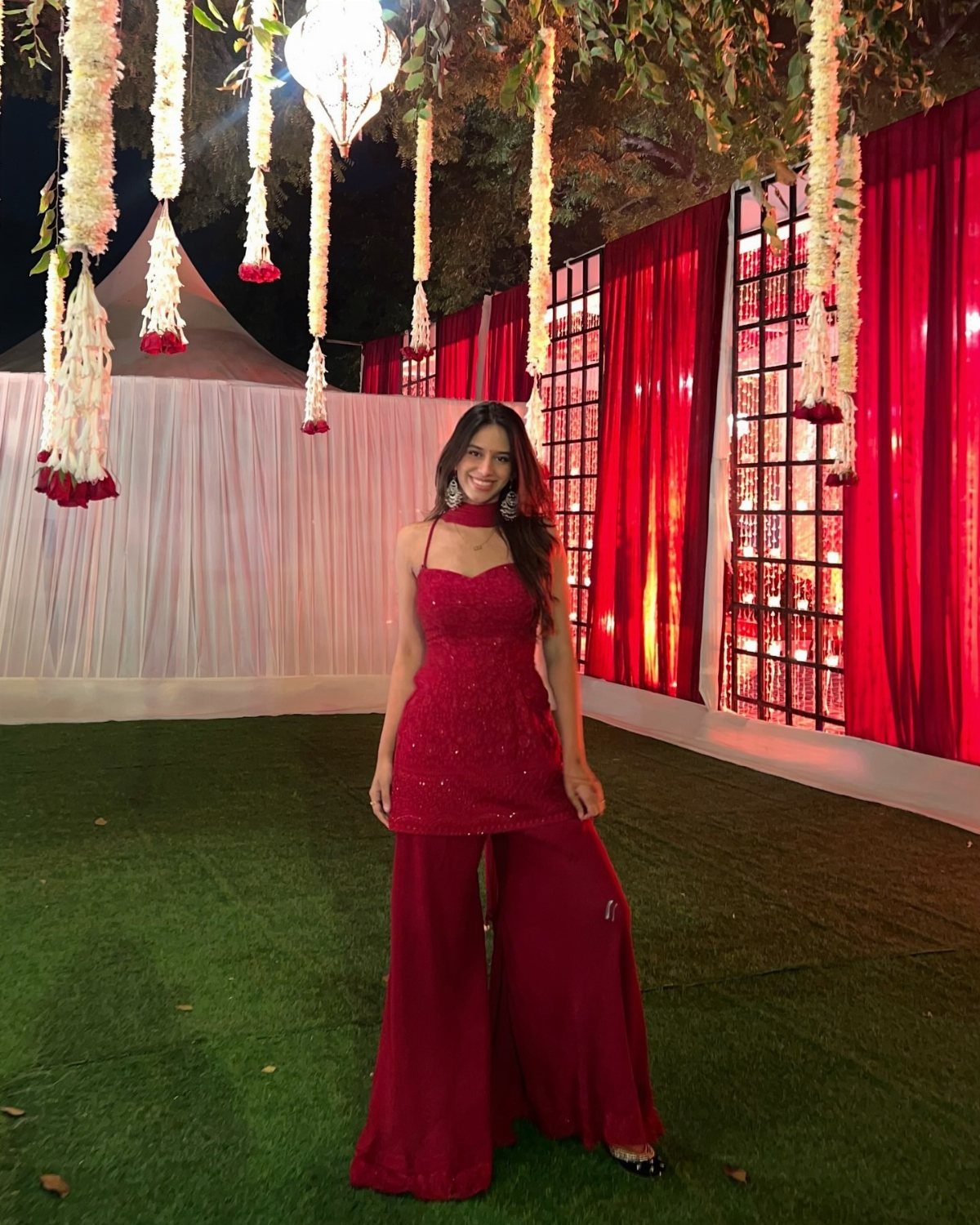 Woman in a maroon sharara set posing against a festive floral backdrop.