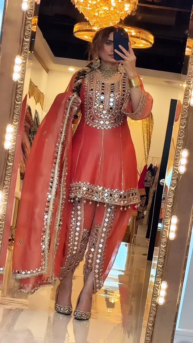 Woman in coral-orange mirror-work tunic and dhoti pants posing for a mirror selfie