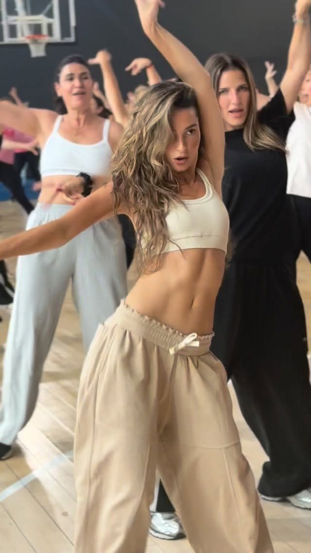 Woman wearing white cropped tank top and beige wide-leg pants in a dance studio.