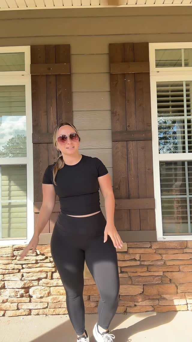 Woman wearing black cropped t-shirt, black leggings, and white sneakers standing outdoors.