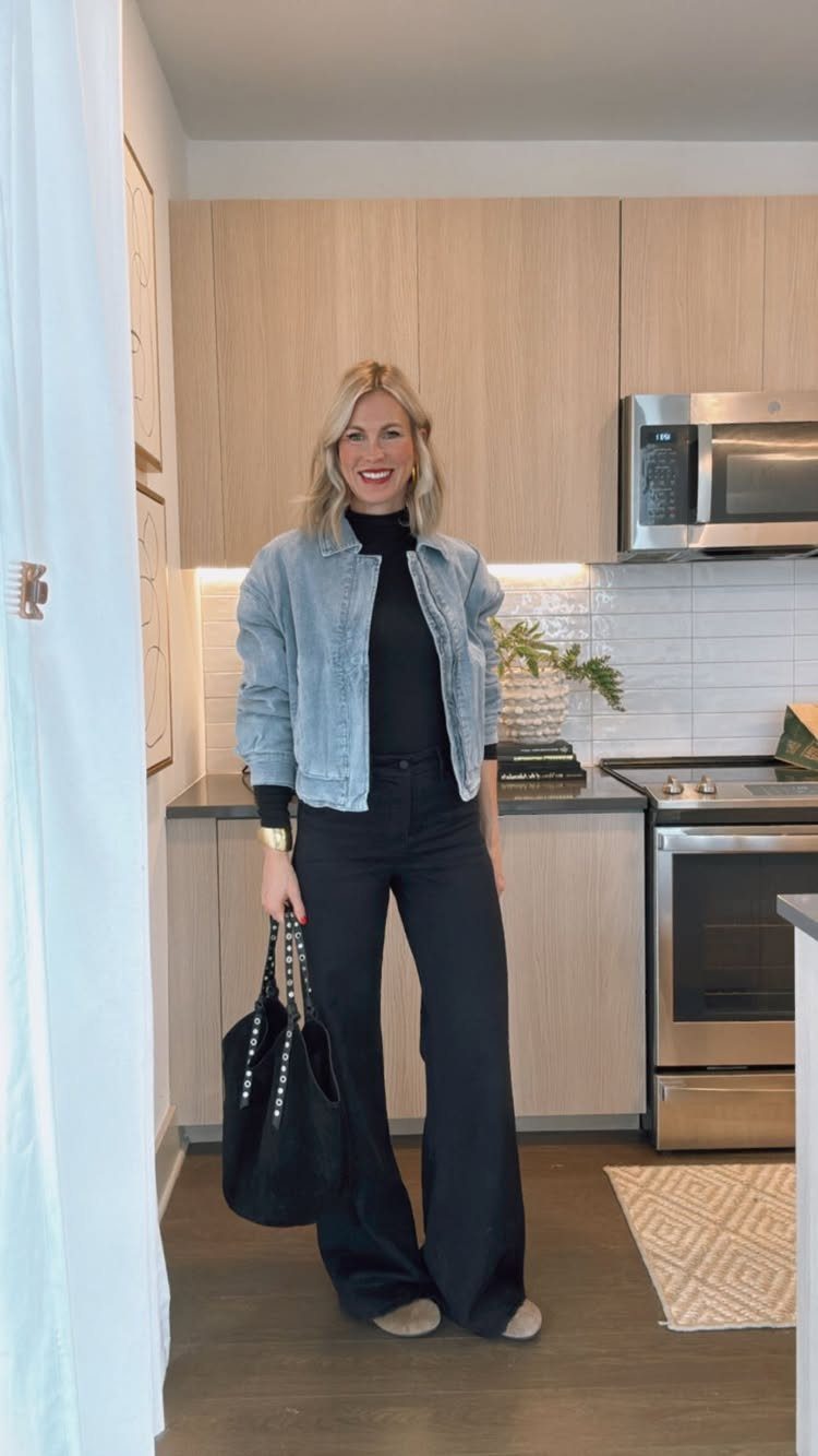 Palazzo Jeans Outfit for Women: 7 Ways to Wear Them 6 Woman wearing a light blue denim jacket and black wide-leg palazzo jeans in a kitchen.