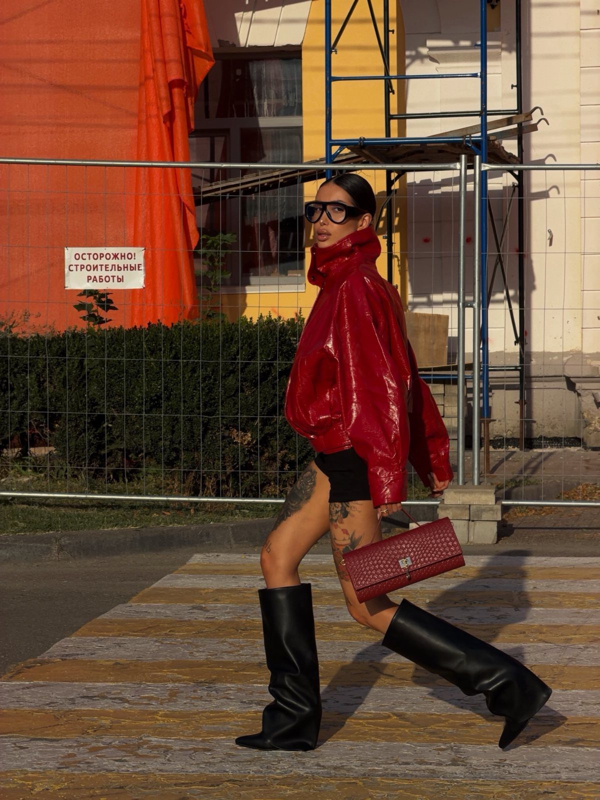 Woman in a glossy deep red oversized jacket and black boots walking outdoors.