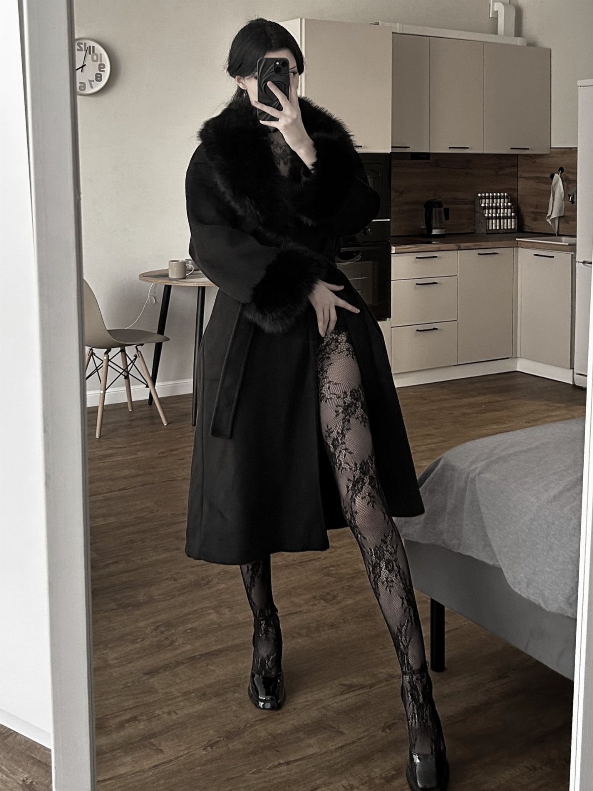 Person in a long black coat with fur collar and lace tights