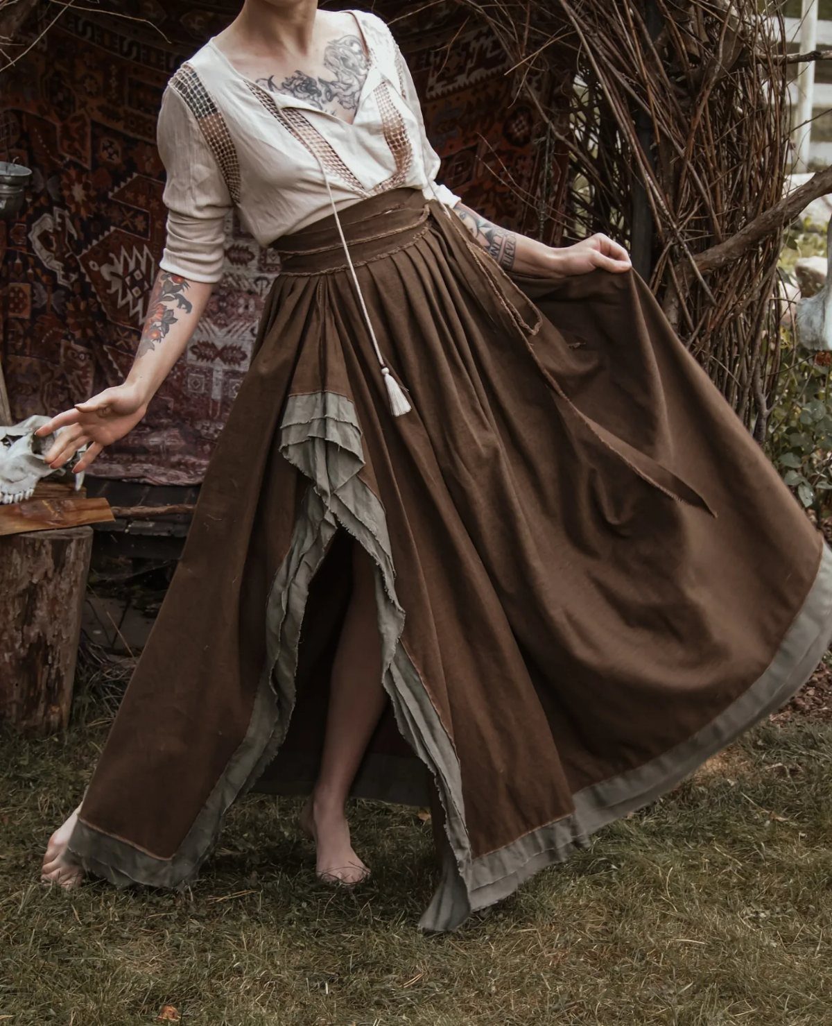 Person in a cream blouse and long brown layered skirt standing outdoors on grass.