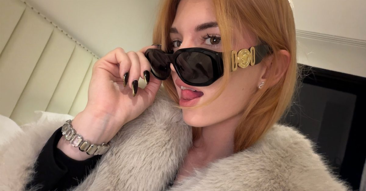 Woman with reddish-blonde hair wearing black sunglasses and a white faux-fur coat.