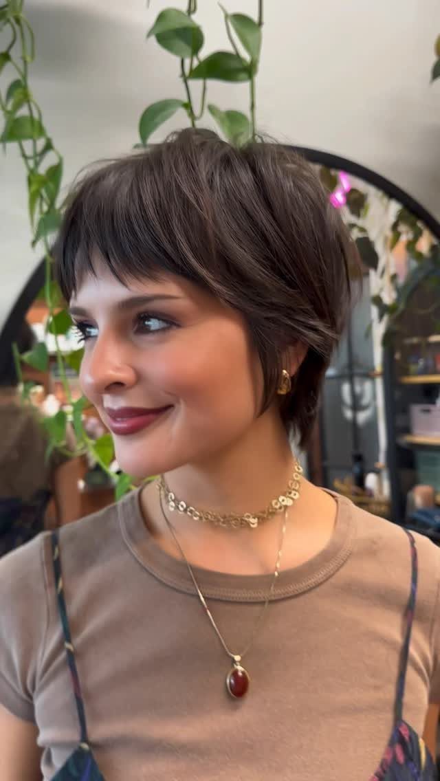 19 Short Pixie Cuts Over 40 With Styling and Color Tips 11 Woman with a brown pixie haircut and wispy bangs wearing gold necklaces.