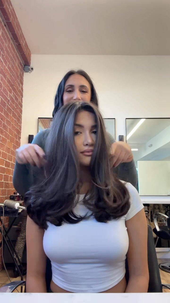 16 Shoulder Length Layered Hair Ideas for Every Texture 7 Woman with voluminous brown shoulder-length layered hair being styled in a salon.